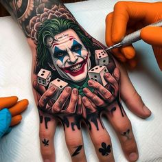 a man with tattoos on his hand holding dices and wearing a joker mask painted on it