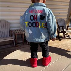 a little boy wearing a jean jacket with mickey mouse patches on it and red shoes