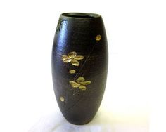 a black vase with gold flowers painted on the outside and inside, sitting on a white surface