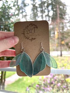 a pair of earrings with green leaves hanging from it's earwires in front of a window