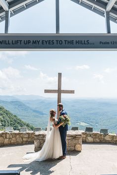 a bride and groom standing in front of a cross with the words will lift up my eyes to the hills