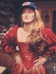 a woman with long hair wearing a red dress and baseball cap standing next to a table