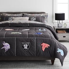 a bed covered in black comforter and pillows with embroidered animals on it, next to a night stand