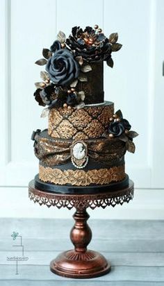 a black and gold wedding cake with flowers on top