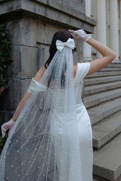 a woman in a white dress and veil is standing on some steps with her hands behind her head