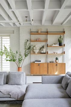 a living room with white brick walls and wooden shelves on the wall next to a gray couch