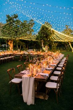 a long table set up with white linens and candles for an outdoor dinner party