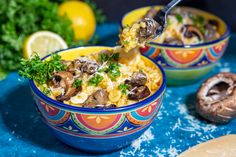 two bowls filled with pasta and mushrooms on top of a blue table next to sliced lemons