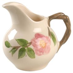 a white ceramic pitcher with pink flowers painted on the side and brown wood handles,