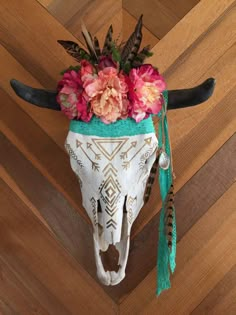 a cow's skull with flowers and feathers on top of it sitting on a wooden floor