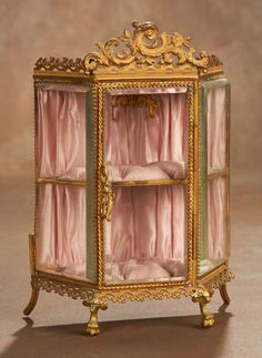 an ornate display case with pink curtains and gold trimmings on the sides,