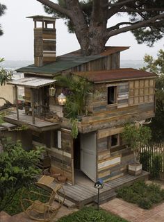 an old wooden house built into the side of a tree with lots of greenery