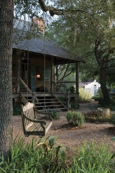 a wooden bench sitting in front of a tree next to a house with a porch