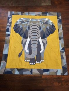 an elephant is depicted on a yellow and gray quilted piece of art that sits on a wooden floor