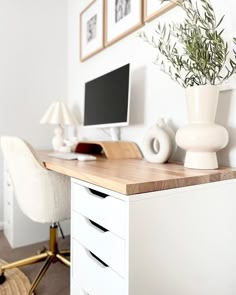 a white desk topped with a computer monitor next to a chair and potted plant