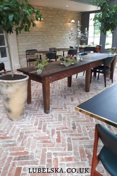 a table and chairs in a room with brick flooring, potted plants on the tables