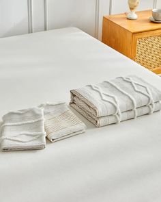 two folded towels on top of a bed next to a night stand and nightstands