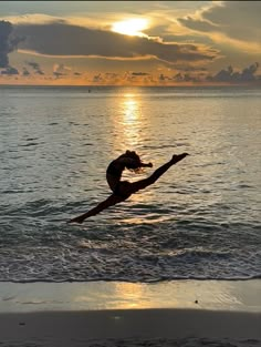 a woman in the water doing a dance move on the beach at sunset or sunrise