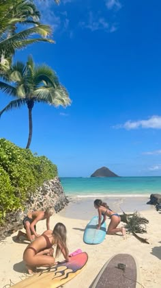 two women in bikinis sitting on the beach next to surfboards and palm trees