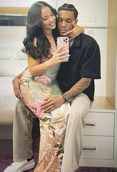 a man and woman sitting next to each other in front of a bed holding a cell phone