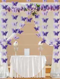 the table is set up with purple butterflies on it and white flowers in vases