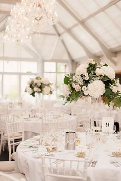 a room filled with tables and chairs covered in white table cloths topped with centerpieces