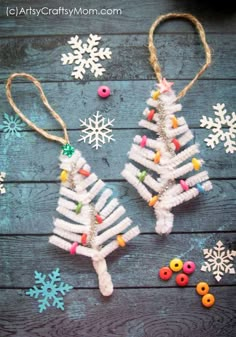 two christmas trees made out of toilet rolls and buttons on a wooden table with snowflakes