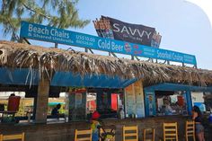 people are standing in line at the beach chairs and cold beer stand with thatched roof