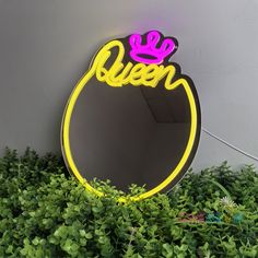 a neon sign with the word queen on it in front of some bushes and plants