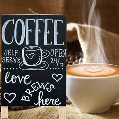 a cup of coffee sitting on top of a table next to a chalkboard sign