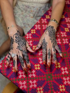 a woman's hands with henna tattoos on her left arm and hand, sitting at a table