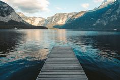 a wooden dock sitting in the middle of a body of water next to some mountains