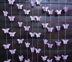 purple paper butterflies hanging from strings on a wooden wall with string attached to the fence