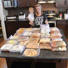 a woman holding a baby standing in front of a table full of bags of food