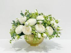 a gold vase filled with white flowers and greenery