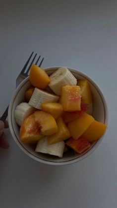 a white bowl filled with cut up fruit and a fork on top of a table