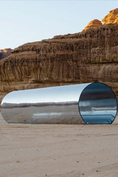 a large metal object sitting on top of a sandy beach next to a mountain range