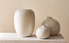 three white vases sitting on top of a table next to each other in front of a beige wall