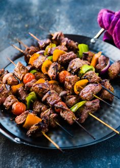 skewers of meat and vegetables on a plate with purple cloth next to it