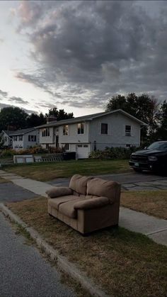 a couch sitting on the side of a road in front of a house at dusk