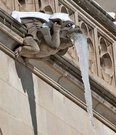 a gargoyle sculpture on the side of a building with ice hanging from it's sides