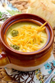 a bowl filled with broccoli cheese soup on top of a table next to bread