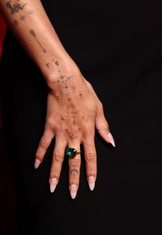 a woman's hand with tattoos and a ring on her left wrist, holding onto an emerald stone