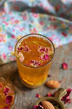 a glass filled with liquid next to some nuts and flowers on a tableclothed cloth