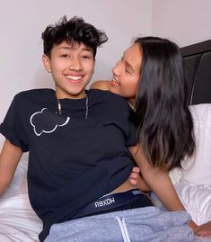 two people laying in bed and one is hugging the other's head while smiling