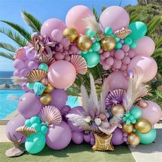 an arrangement of balloons and seashells on the ground near a swimming pool with palm trees