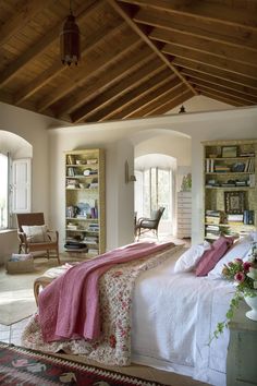 the bedroom is decorated in white and has pink accents on the bedspread, along with bookshelves