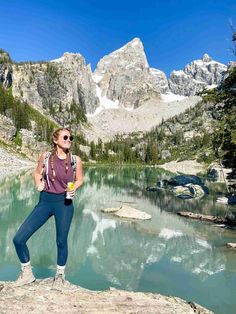 a woman standing on top of a rock next to a lake