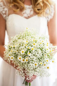 a bride holding a bouquet of daisies and baby's breath