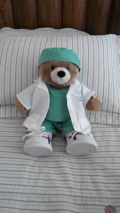 a teddy bear dressed as a doctor sitting on a bed